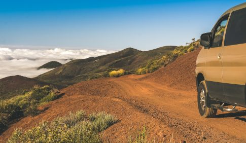 Off road vehicle on a mountain path. Blue sky, clouds and a beautiful panorama on the background. 4x4 van on a dirt road. Suv climbing on a tourist rural way Travel adventure and open air trip concept